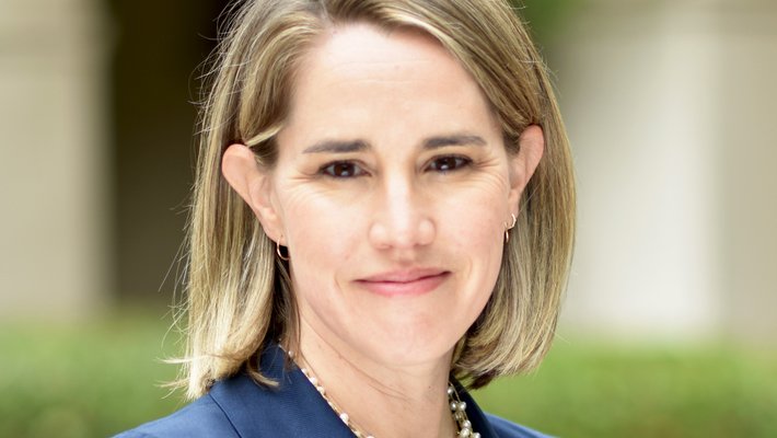 A photo portrait of a woman with blond hair wearing a blue blazer and black shirt with a chunky pearl necklace.