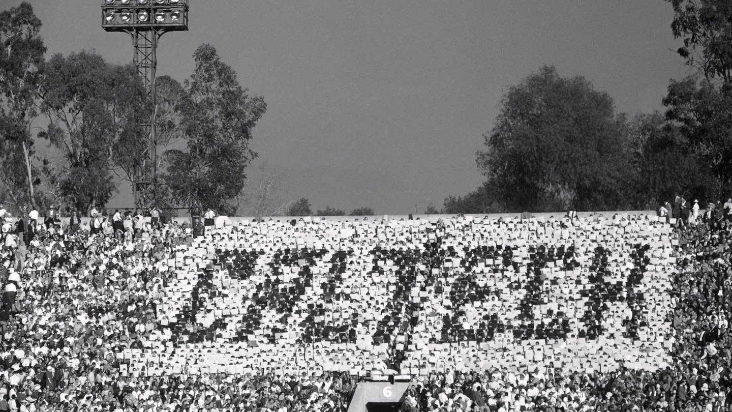 This black and white photo shows the packed stadium for the 1961 Rose Bowl Game. At center, thousands of fans hold cards over their heads that combine to read "CALTECH" in block letters.