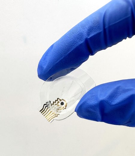 a small clear device with microfluidic components visible is pinched between two fingers in blue plastic gloves