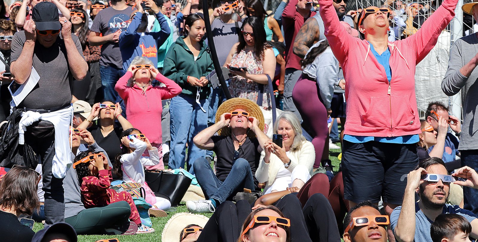 A densely gathered crowd wearing eclipse glasses and looking upward