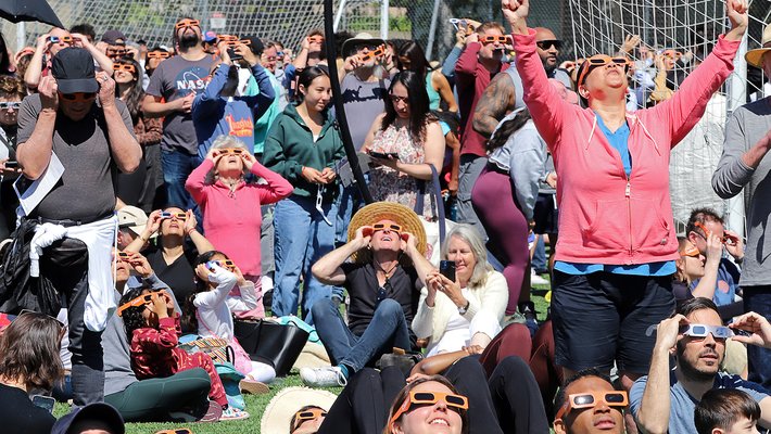 A densely gathered crowd wearing eclipse glasses and looking upward