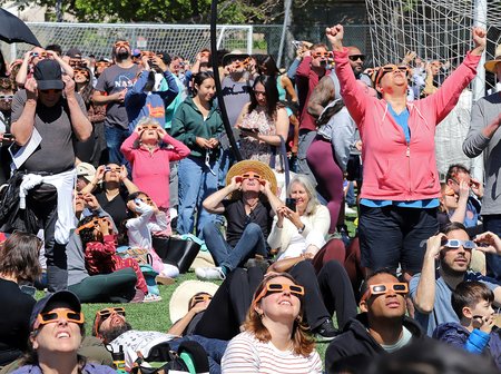 A densely gathered crowd wearing eclipse glasses and looking upward