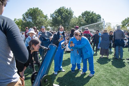 a crowd of people gathered around a solar telescope on an athletic field