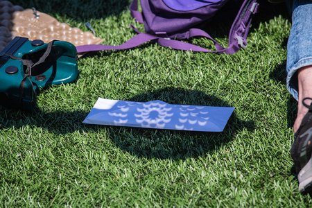 a colander is placed over a white envelope on grass, casting crescent moon-shaped shadows