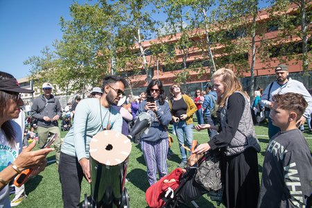 a man on a field setting up a solar telescope on a tripod, surrounded by people gathered to see the solar eclipse