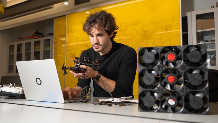 Alejandro Stefan-Zavala sits in front of a laptop with a drone in hand and small fans off to his side.