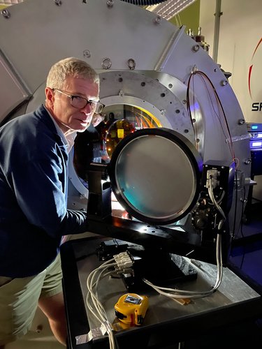 Researchers stands in front of chamber in a lab.