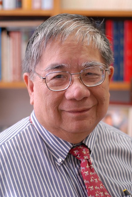 Sunney Chan wears a shirt and tie and smiles at the camera in this portrait. Bookshelves can be seen in the background.