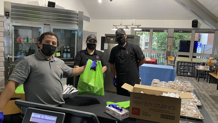 Three masked staffers prepare bags of food.