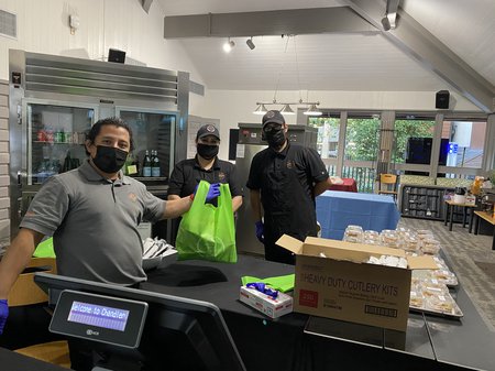 Three masked staffers prepare bags of food.