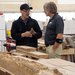In a workshop, two men stand alongside slabs of oak
