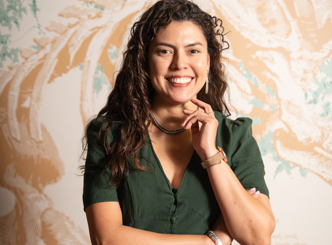 A woman in a green dress smiles for a photo in front of an illustration of a fossil