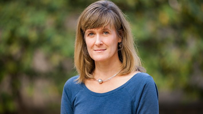 A portrait of Tracy Dennison. She is outside and bushes are in the background.