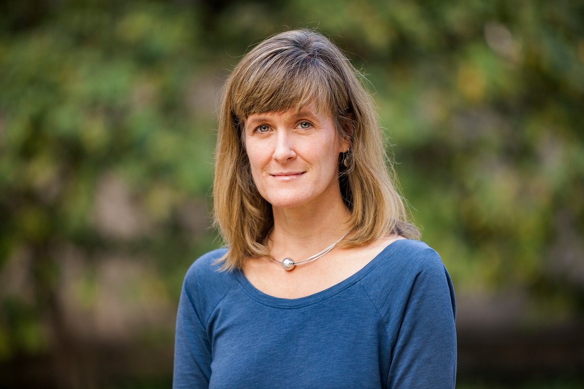 A portrait of Tracy Dennison. She is outside and bushes are in the background.