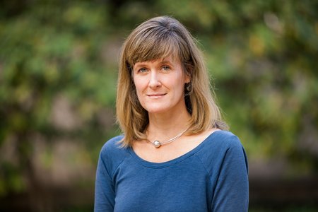 A portrait of Tracy Dennison. She is outside and bushes are in the background.