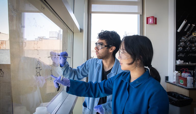 woman and man in lab coats work at whiteboard