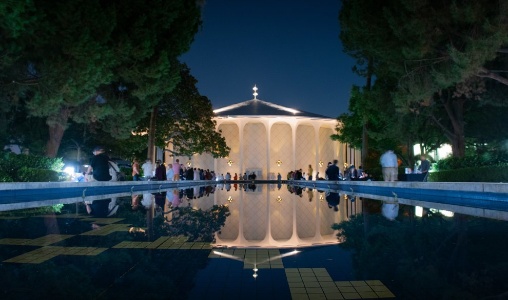 Beckman Auditorium is reflected in the Gene Pool on the Caltech campus as audience members mingle, eat, and stop at informational booths arranged on either side of the pool