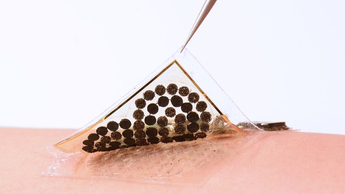 A pair of tweezers peels a sample of a electronic skin from the skin of an arm.