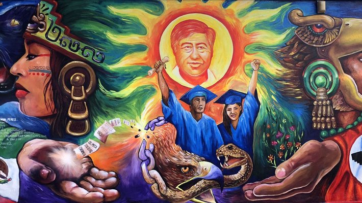 mural showing two graduates in blue gowns with diplomas with an eagle and a snake below them, with Aztec-influenced images, the Mexican flag, and a man with a red flag