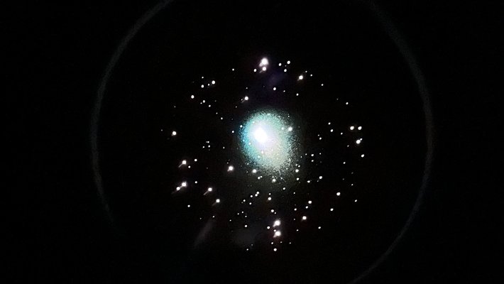 A cluster of stars as seen through a telescope's eyepiece, with a glowing green blob in the middle