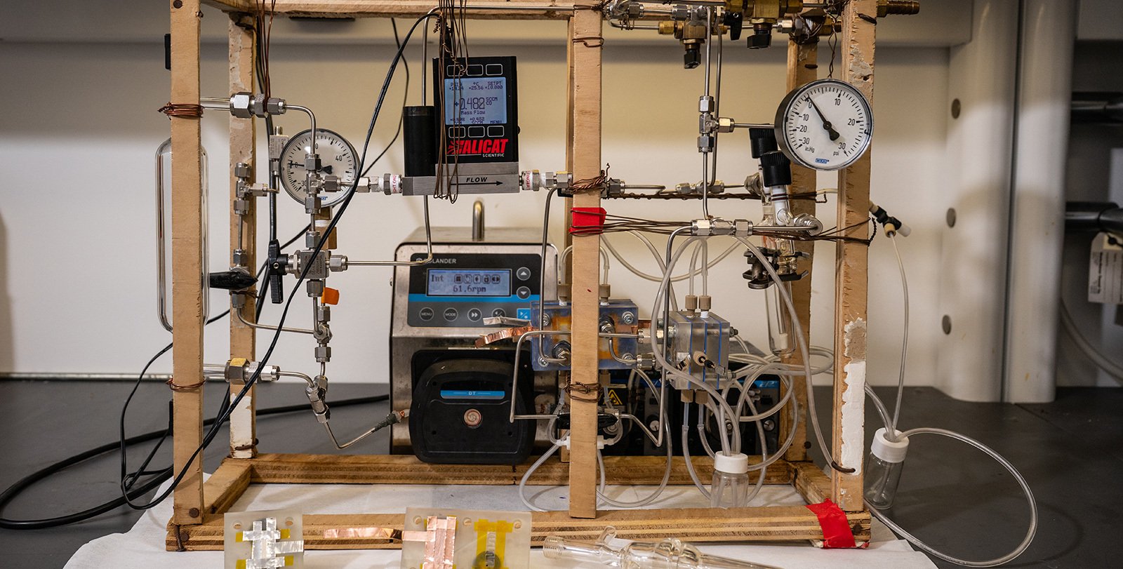 A tabletop system with a wooden frame, tubing, a glass cylinder, gauges, and pumps