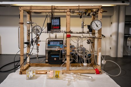 A tabletop system with a wooden frame, tubing, a glass cylinder, gauges, and pumps