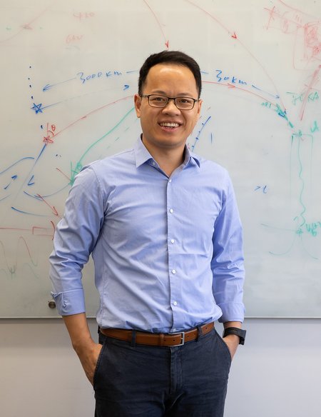 Image of Zhongwen Zhan in light blue shirt standing in front of white board