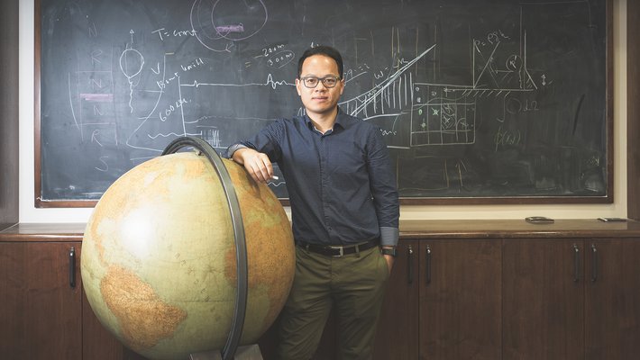 Image of Zhongwen Zhan standing next to a globe in front of a chalk board