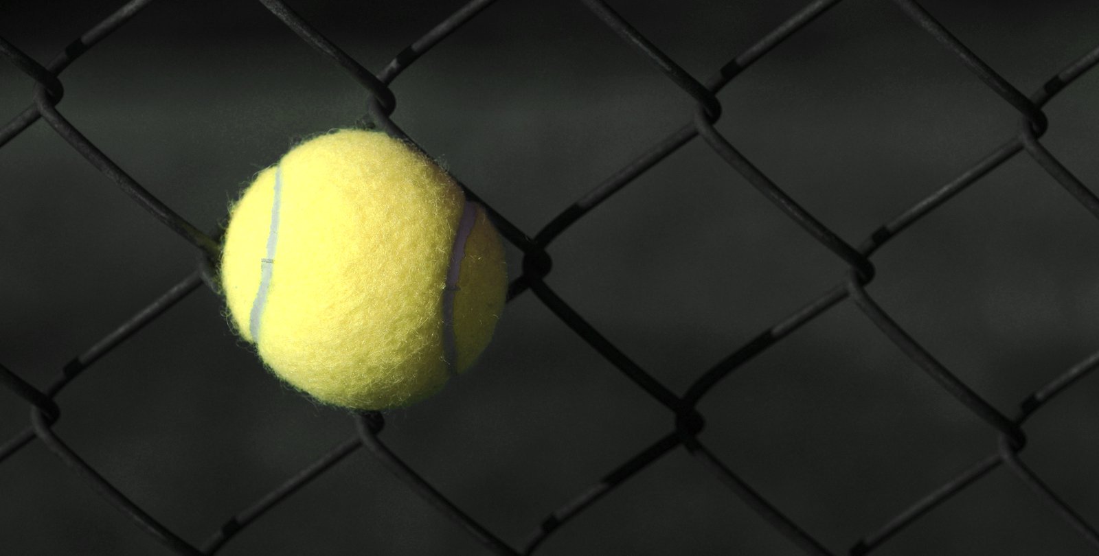 A tennis ball stuck in a chain-link fence.