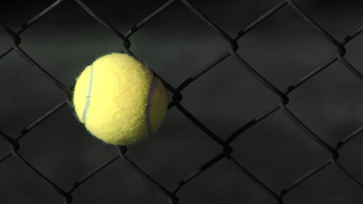 A tennis ball stuck in a chain-link fence.
