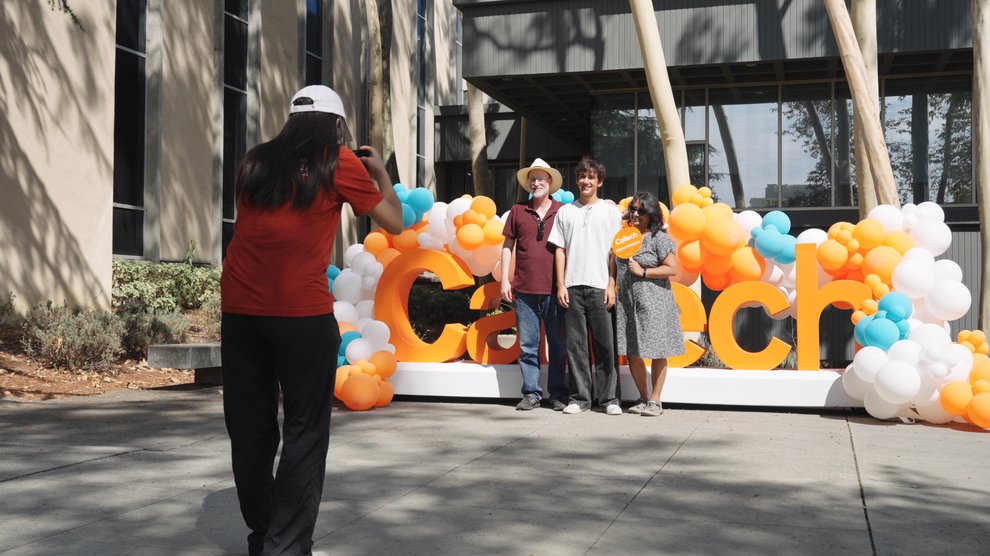 A student takes a picture of another student and their family in front of a Caltech sign.