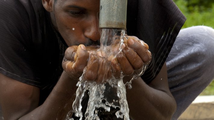 A man cups his hands under a pipe to catch and drink water.