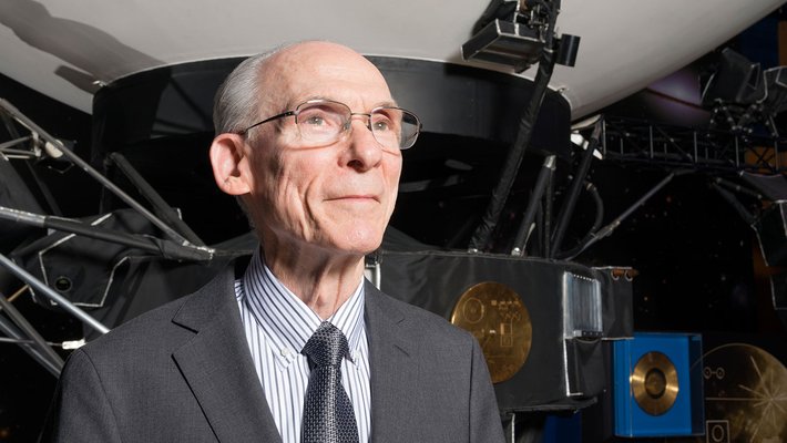 Ed Stone standing in front of a scale-model of the Voyager spacecraft at NASA's Jet Propulsion Laboratory.