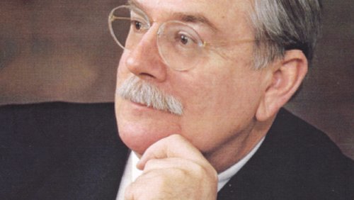 A portrait of David A. Evans. He wears glasses and a suit and has his head turned to one side.