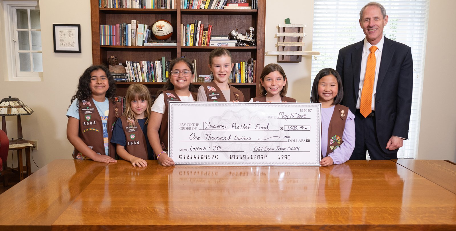 Six Girl Scout Brownies stand with Caltech President Thomas Rosenbaum holding a giant representation of the check they donated