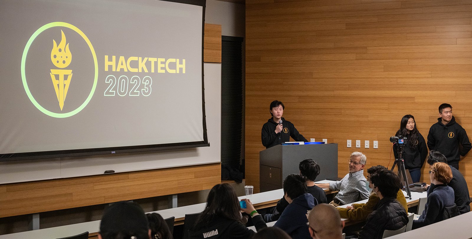 Aaron Zhao speaks in front of a screen that reads "Hacktech 2023"