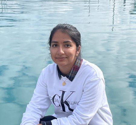 A portrait of Sreemanti Dey. She wears a sweater and sits in front of a body of water.