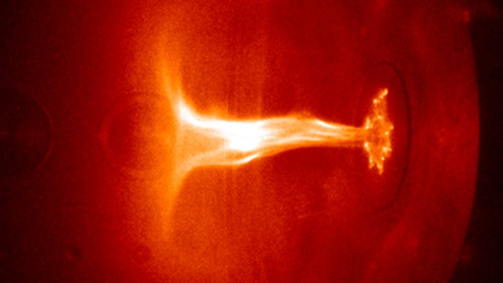 A flame-like jet of plasma takes on a shape reminiscent of an umbrella or mushroom inside a vacuum chamber.