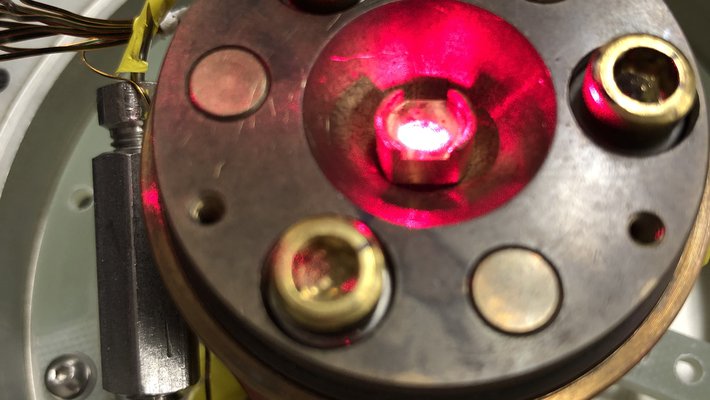 A strong laser is seen illuminating a material in a low-temperature chamber.