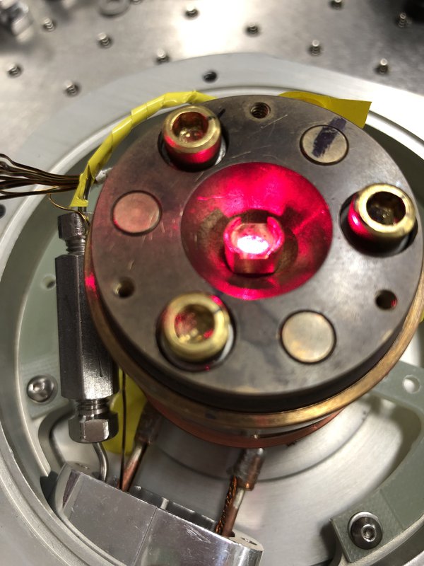A strong laser is seen illuminating a material in a low-temperature chamber.