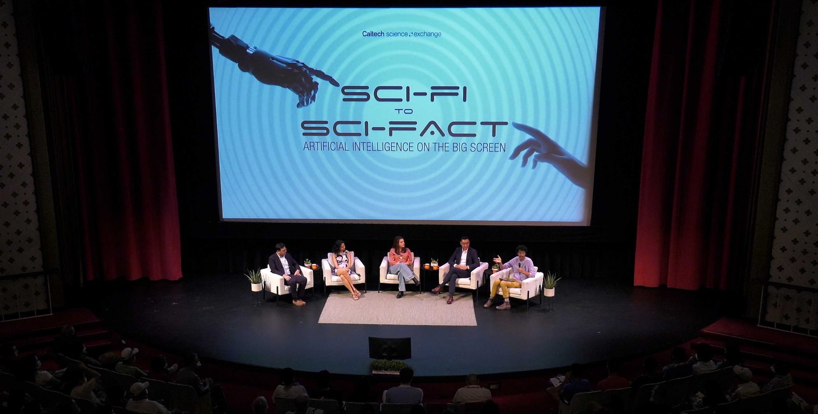 Panelists sit on stage in front of a large screen