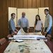 History professor Nicolás Wey-Gómez poses with three students. A series of maps are unfurled on a long table before them