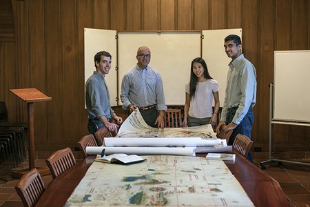 History professor Nicolás Wey-Gómez poses with three students. A series of maps are unfurled on a long table before them