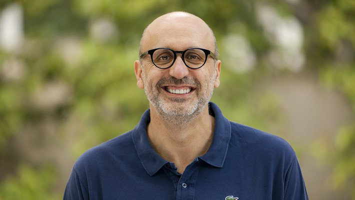A portrait of Antonio Rangel. He wears glasses and a blue polo. Green trees are in the background
