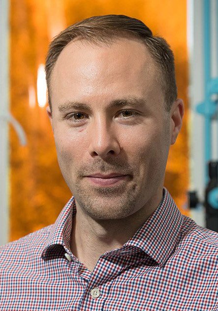 A bust portrait of Maxwell Robb. He has short cropped hair and wears a button-down shirt.