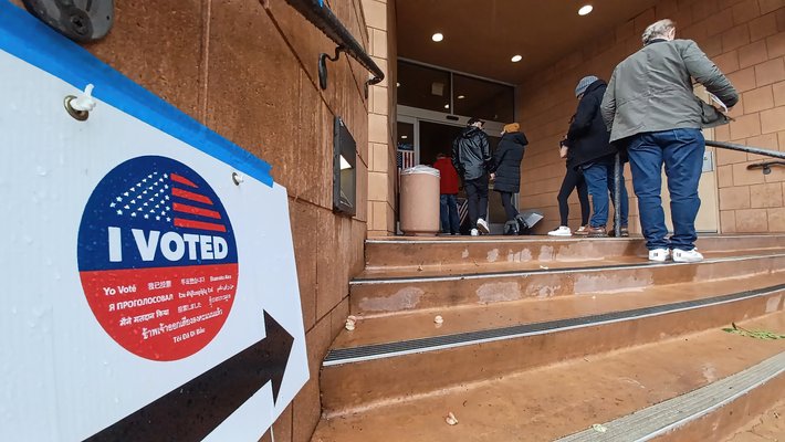 people standing in line outside a voting center entrance