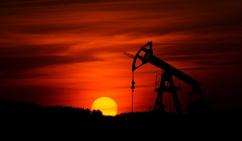 Oil derricks pump as the sun sets in the background