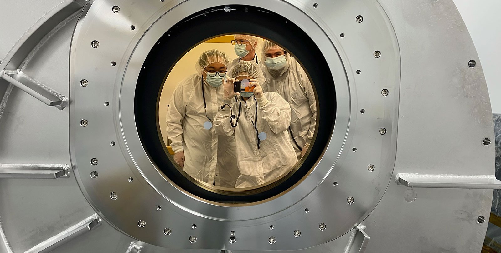 SPHEREx team members can be seen here in a reflection from the chamber's gold-coated, sapphire window.