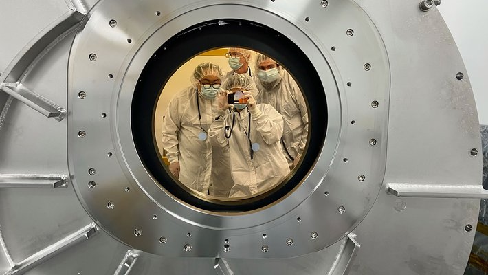 SPHEREx team members can be seen here in a reflection from the chamber's gold-coated, sapphire window.