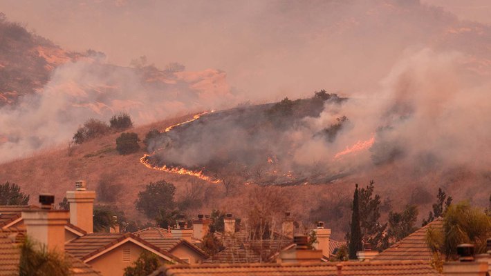 pink and orange image of a wildfire in the hills over a neighborhood